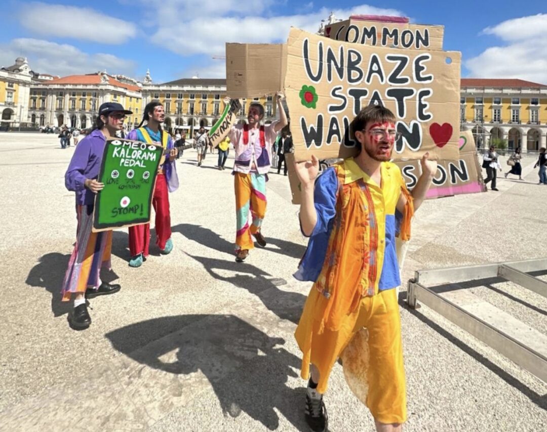 Artistas performativos con traxes de cores e carteis reivindicativos na Praza do Comercio de Lisboa para MEO Kalorama.