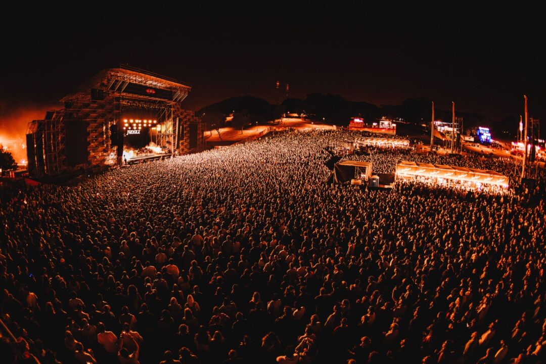 Vista panorâmica noturna de um grande concerto ao ar livre com milhares de pessoas.