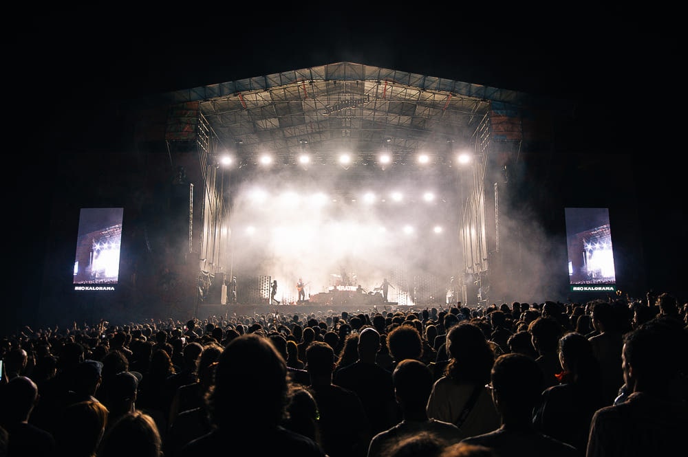 Palco principal iluminado à noite, com a multidão a assistir a um concerto.