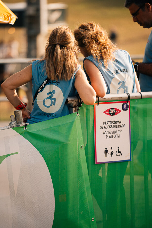 Duas voluntárias com coletes azuis junto à plataforma de acessibilidade do MEO Kalorama.