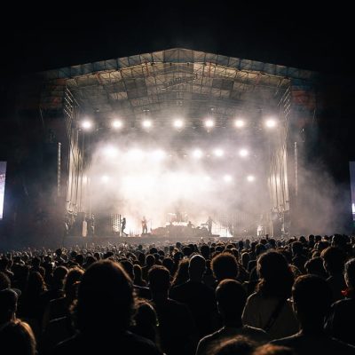 Palco principal iluminado à noite, com a multidão a assistir a um concerto.