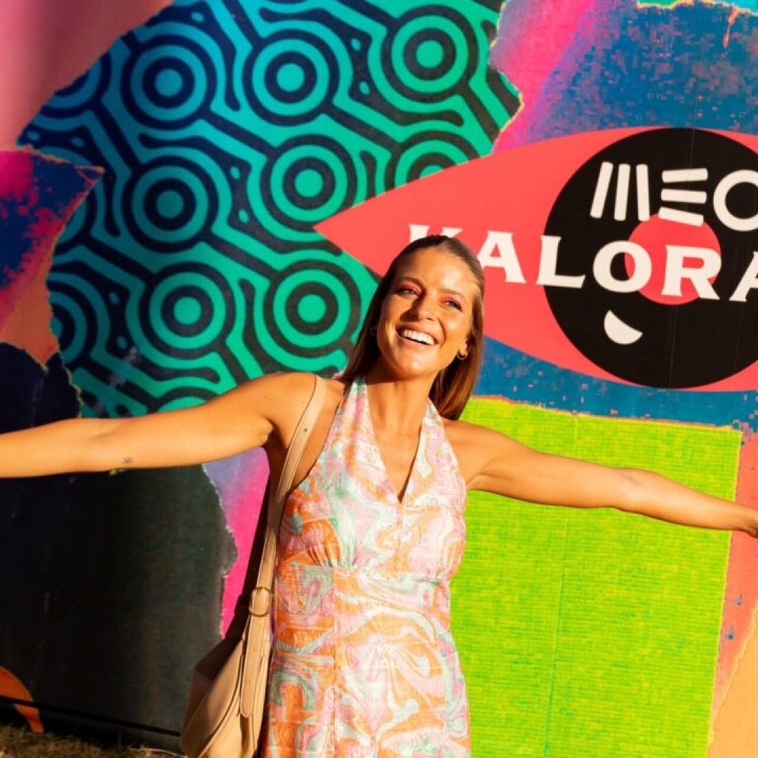 Mulher a sorrir com braços abertos diante de mural colorido com o logótipo MEO Kalorama.