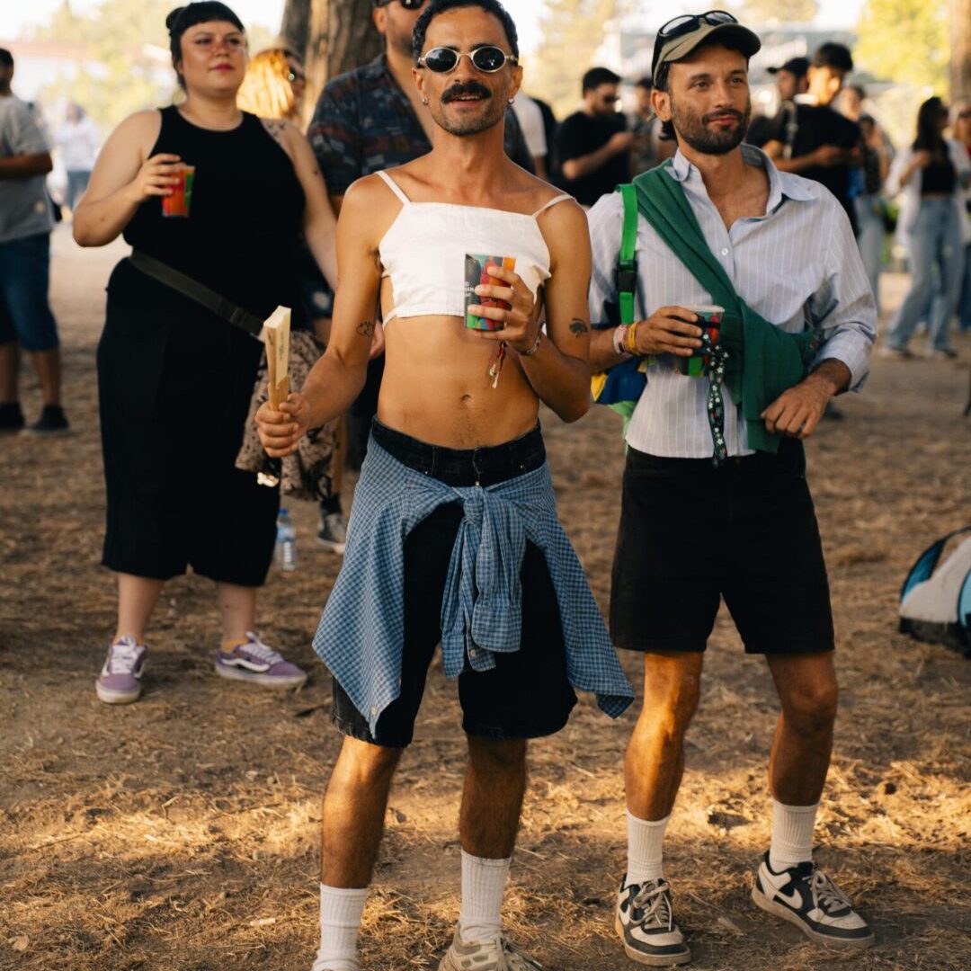 Homem de óculos de sol e top branco a dançar com um copo na mão, entre o público do festival.