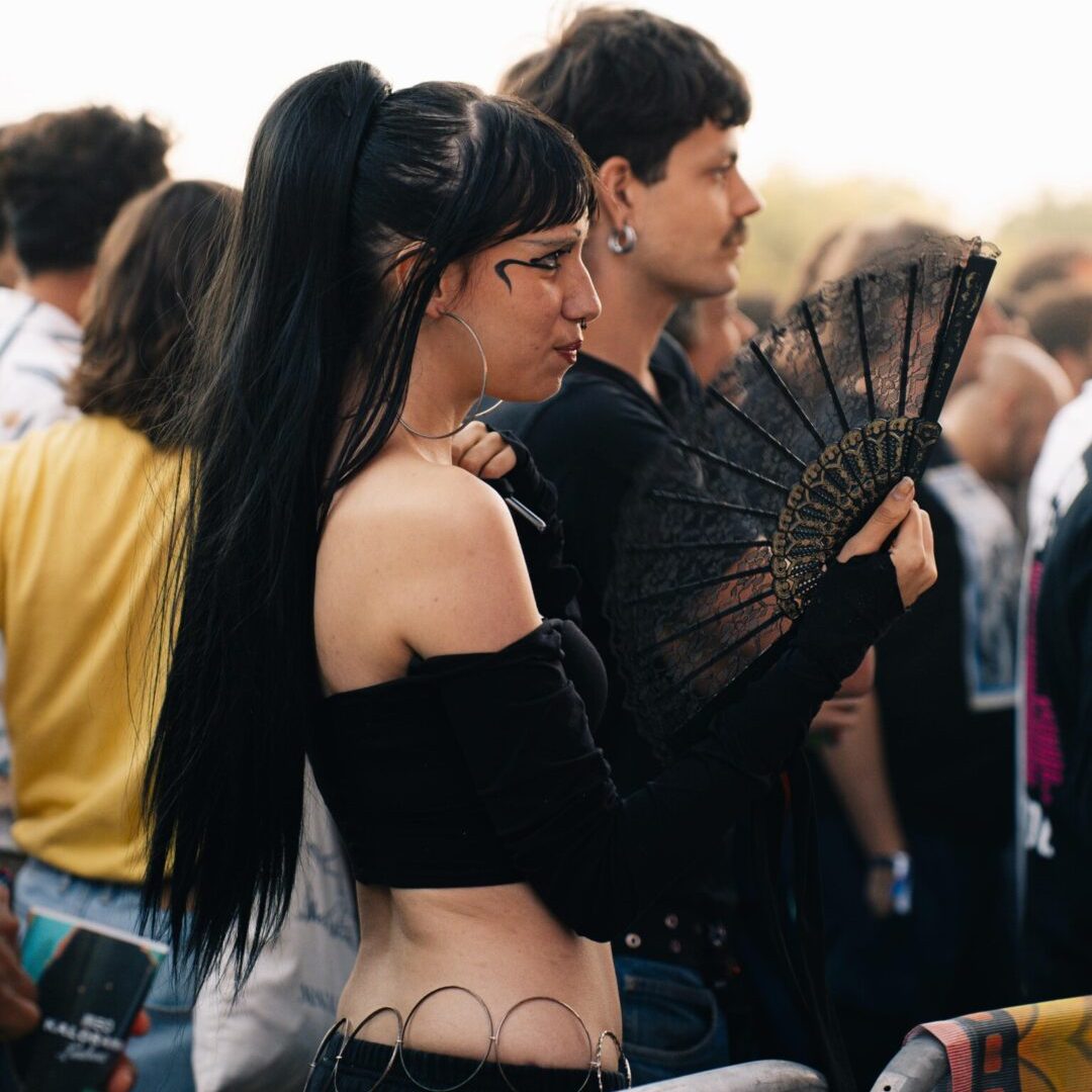 Jovem com top preto e leque decorado junto às grades do público durante o festival MEO KALORAMA.