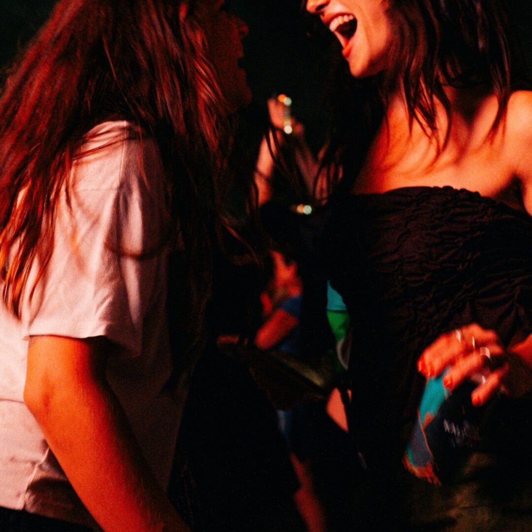 Duas mulheres a sorrir e a dançar juntas à noite durante o festival.